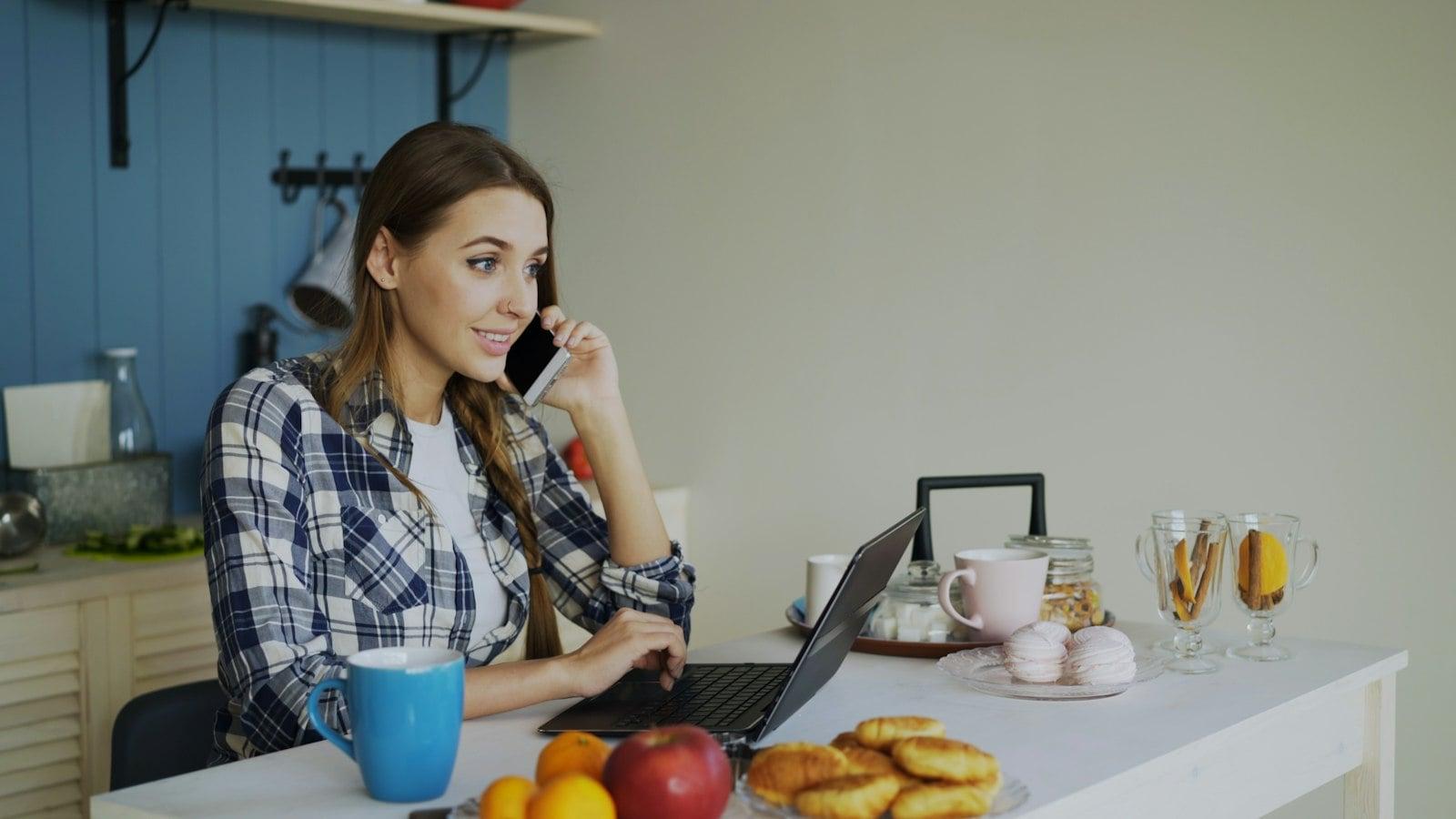 Woman talking on phone while working on laptop at table